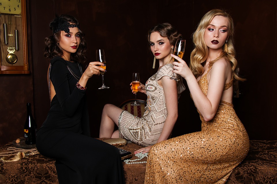 Tři dámy sedící na stole, držící sklenky s nápojem